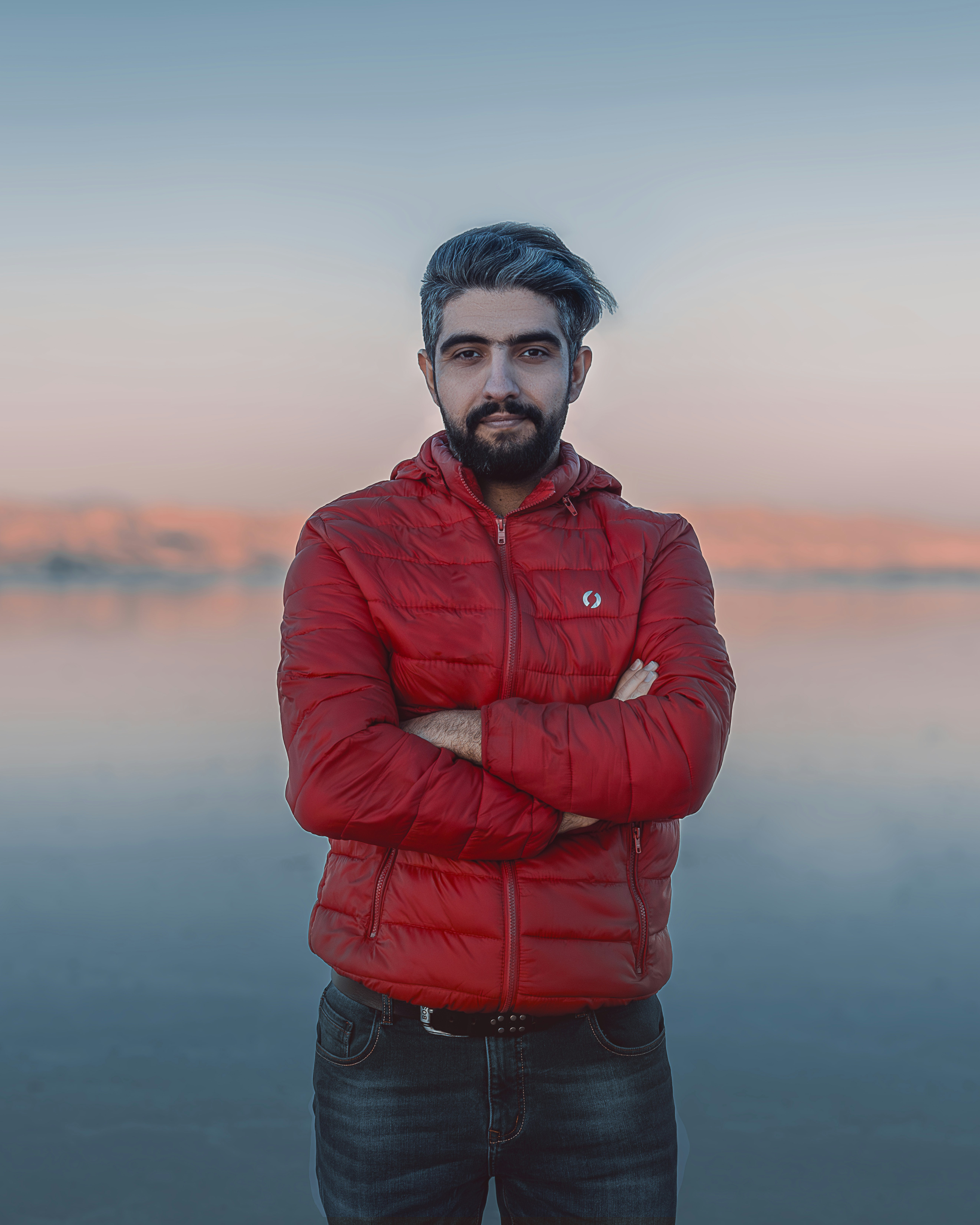 a man with his arms crossed standing in front of a body of water