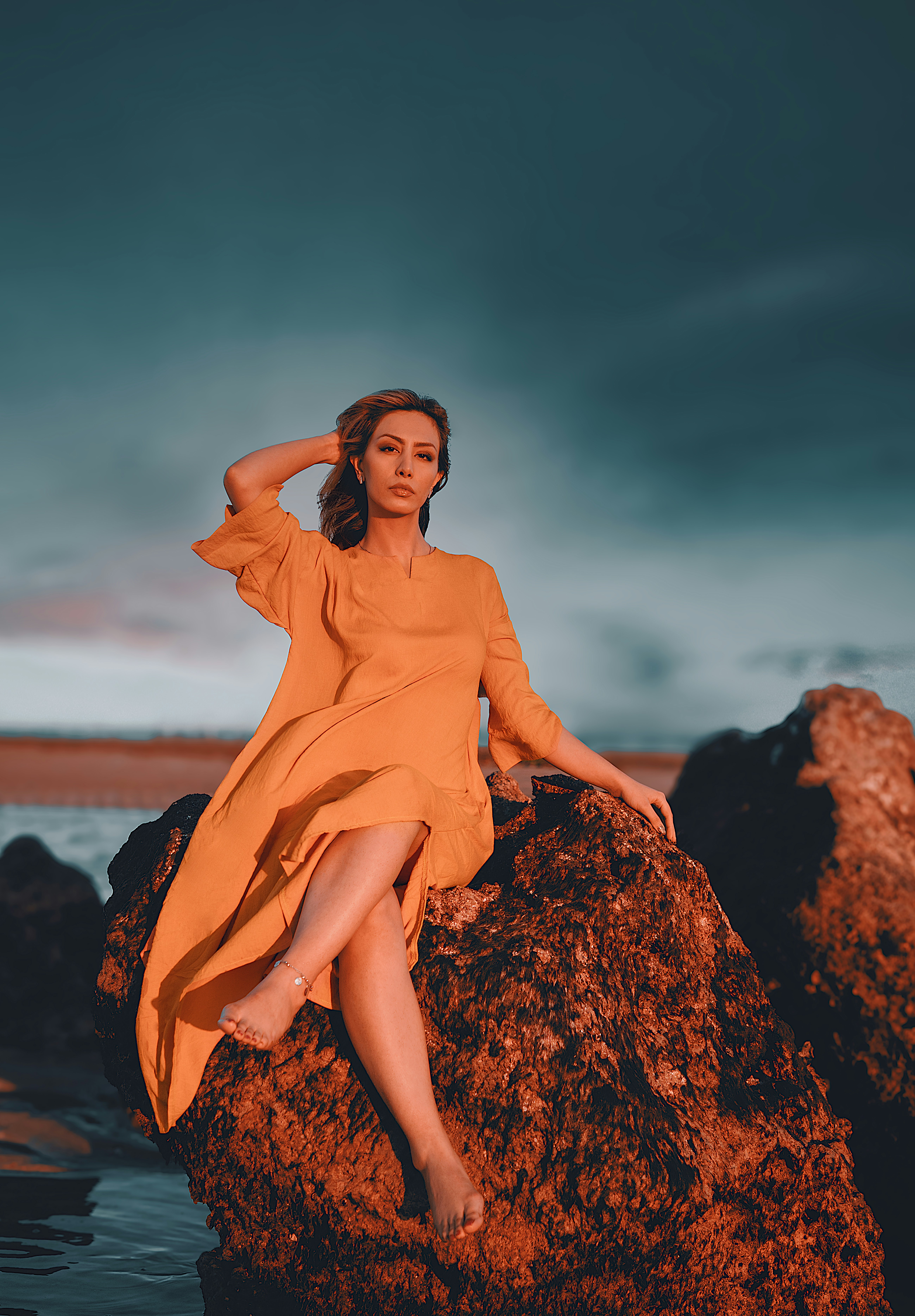 a woman sitting on top of a rock next to a body of water