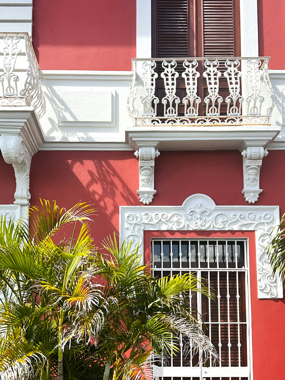 a red and white building with a balcony and palm trees