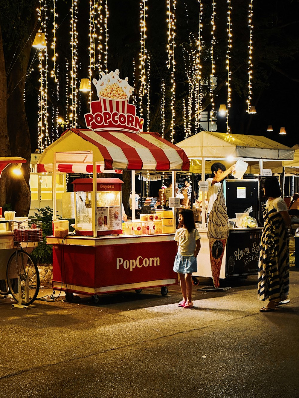 a woman and a child standing in front of a popcorn cart