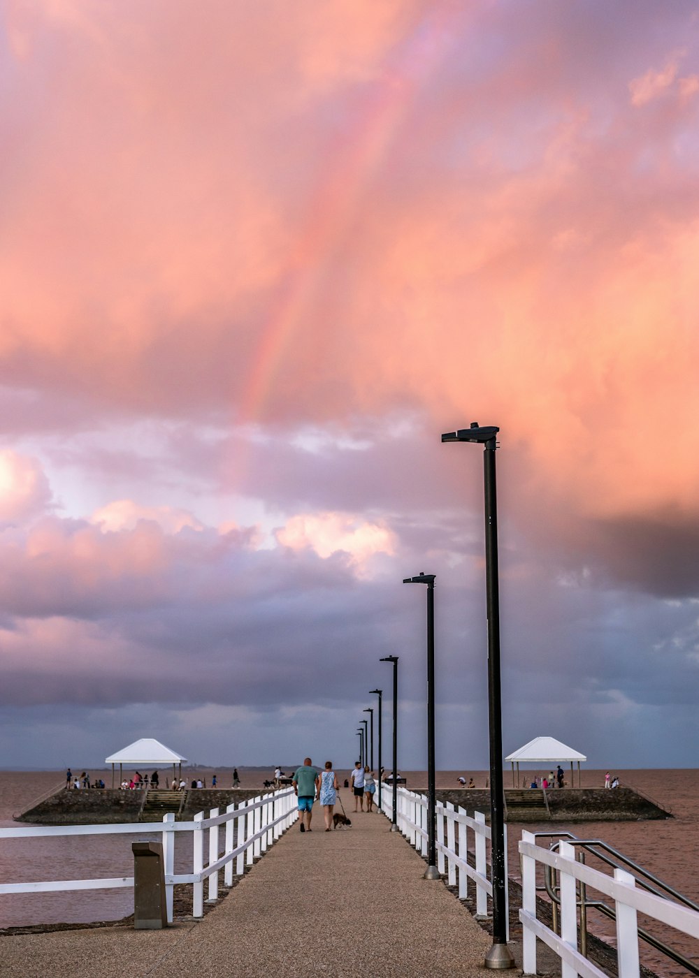 a long pier with a rainbow in the sky