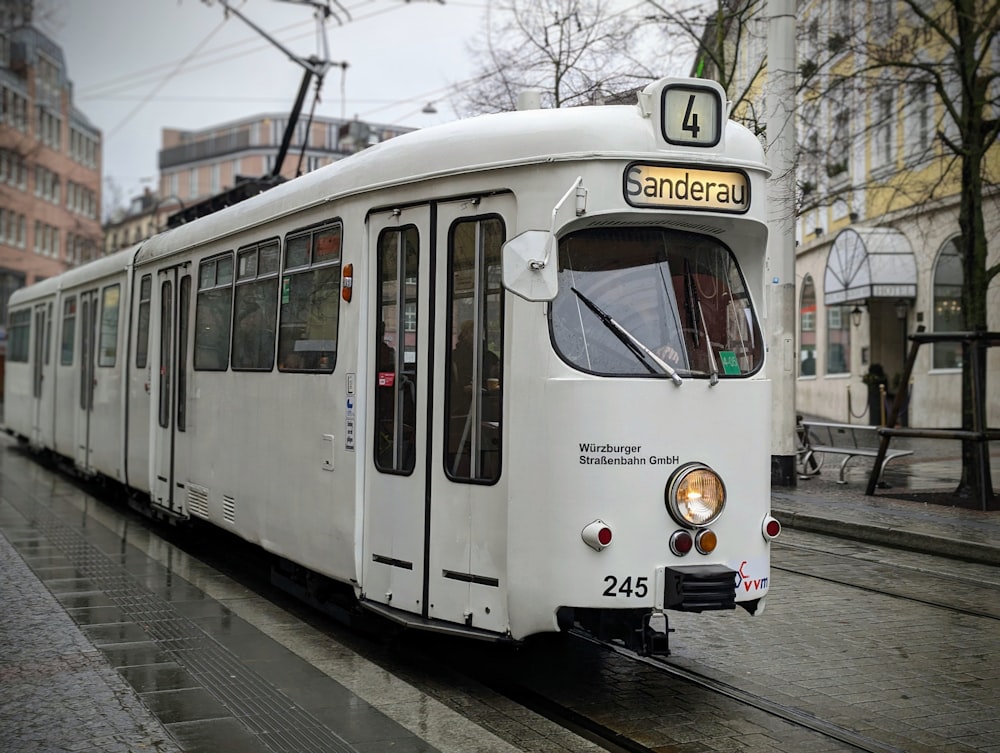 a white train traveling down a street next to tall buildings