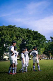 a group of young boys standing on top of a lush green field