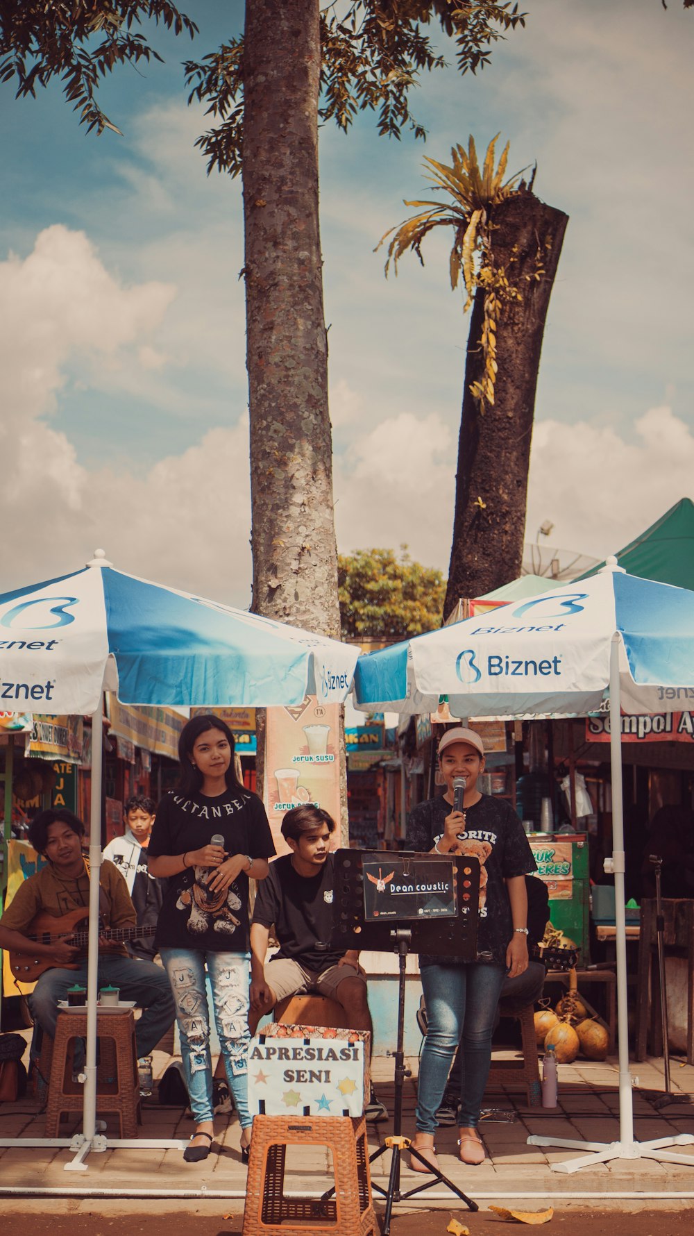 a group of people sitting under umbrellas under a tree