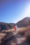 a man and woman standing on top of a dry grass covered hillside