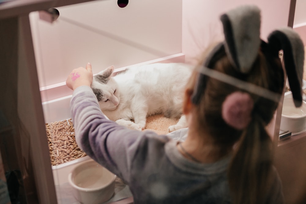 a little girl petting a cat in a cage