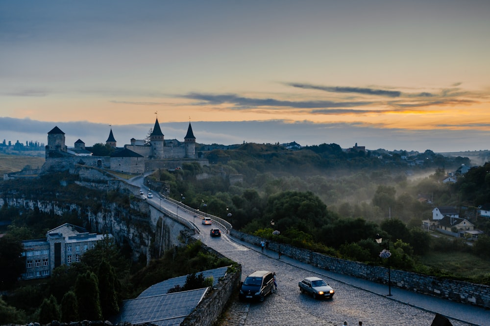 a group of cars driving down a road next to a castle