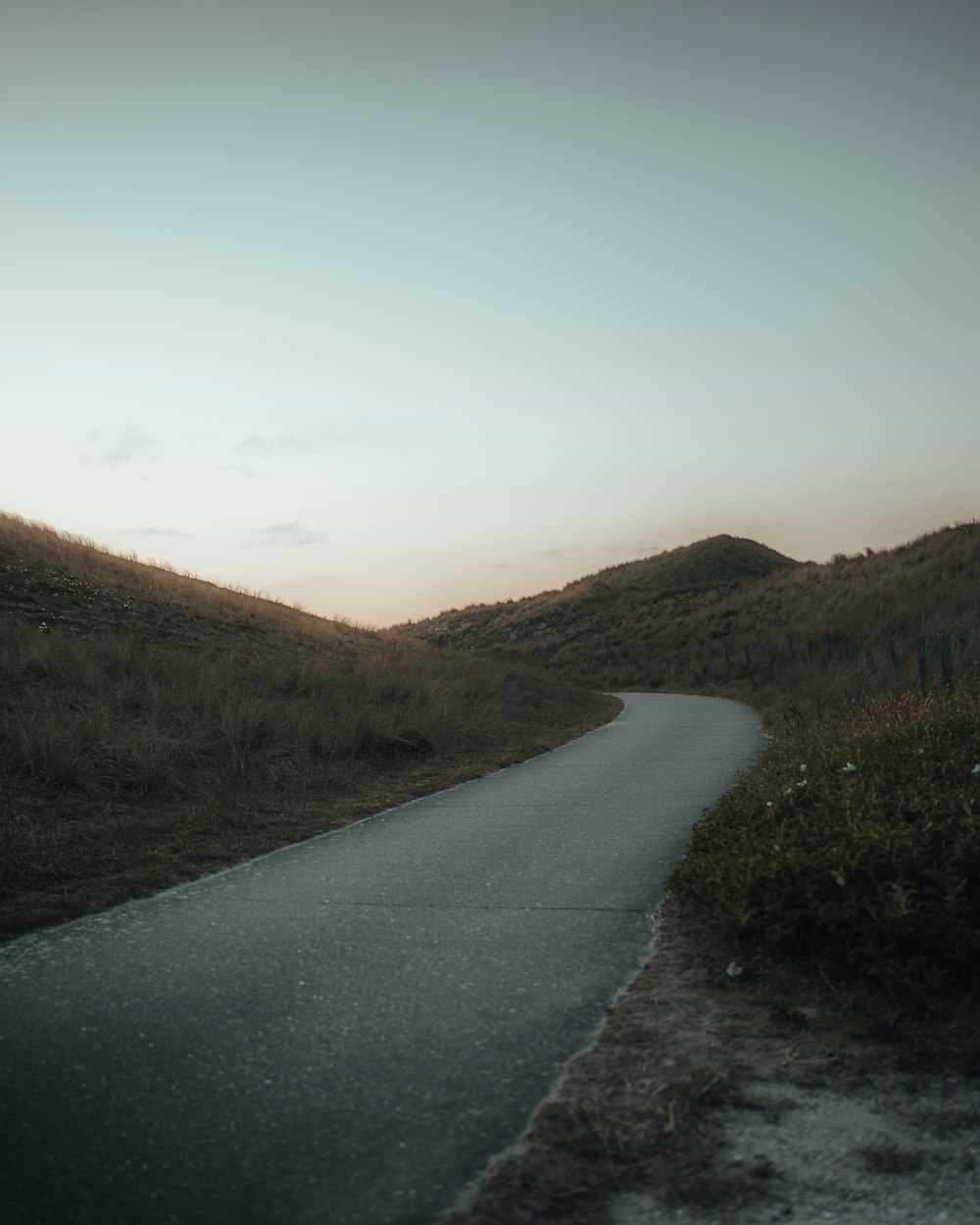 an empty road in the middle of a grassy hill