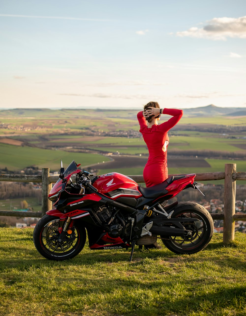 a woman in a red dress standing next to a red motorcycle