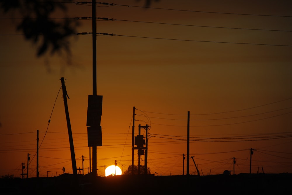 the sun is setting behind power lines and telephone poles