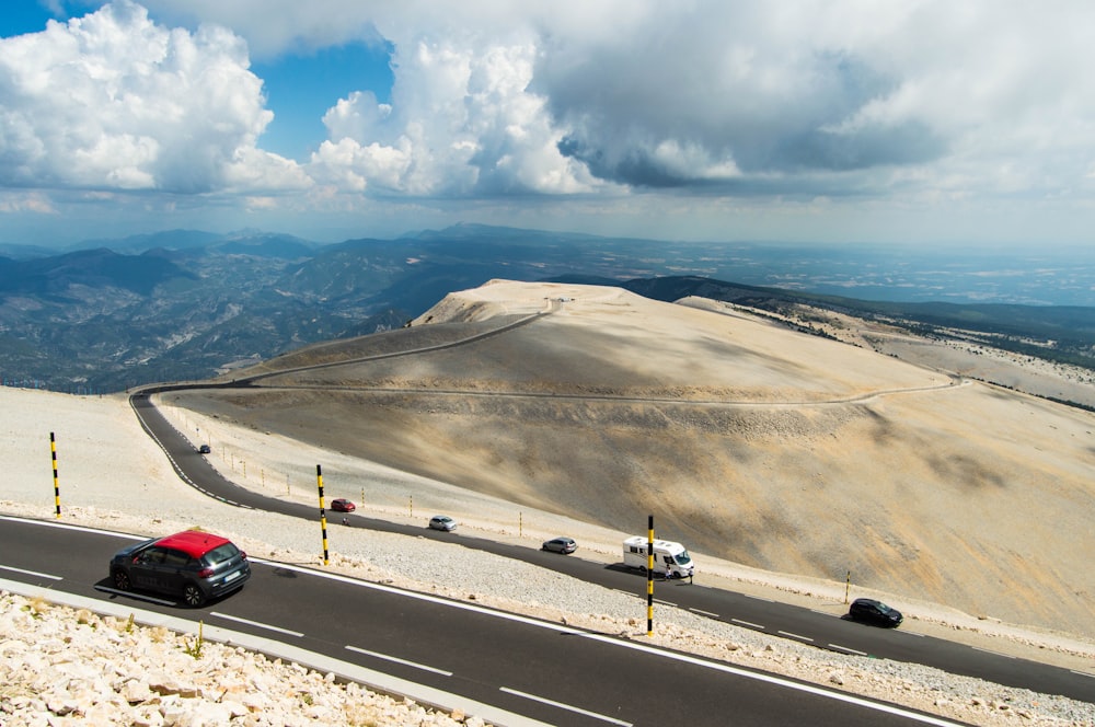 a red car driving down a road next to a mountain