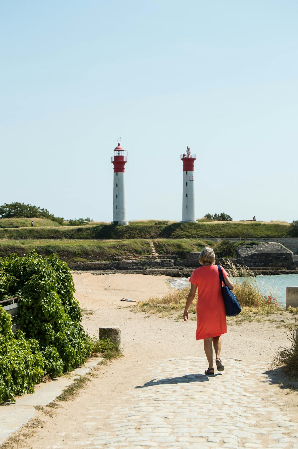 a woman in a red dress is walking towards two lighthouses