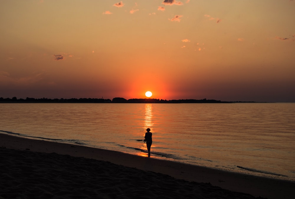 una persona de pie en una playa al atardecer