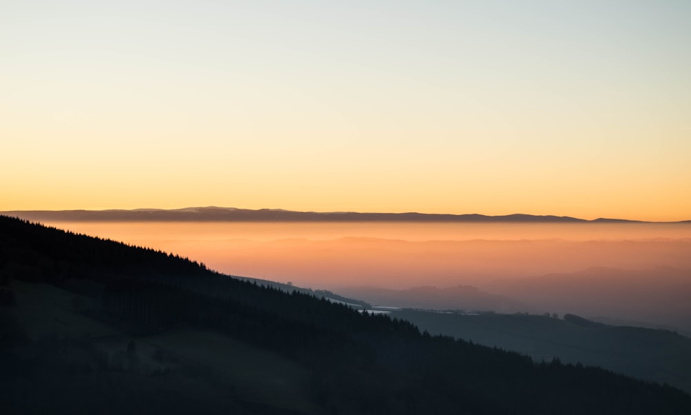 the sun is setting over the mountains with fog