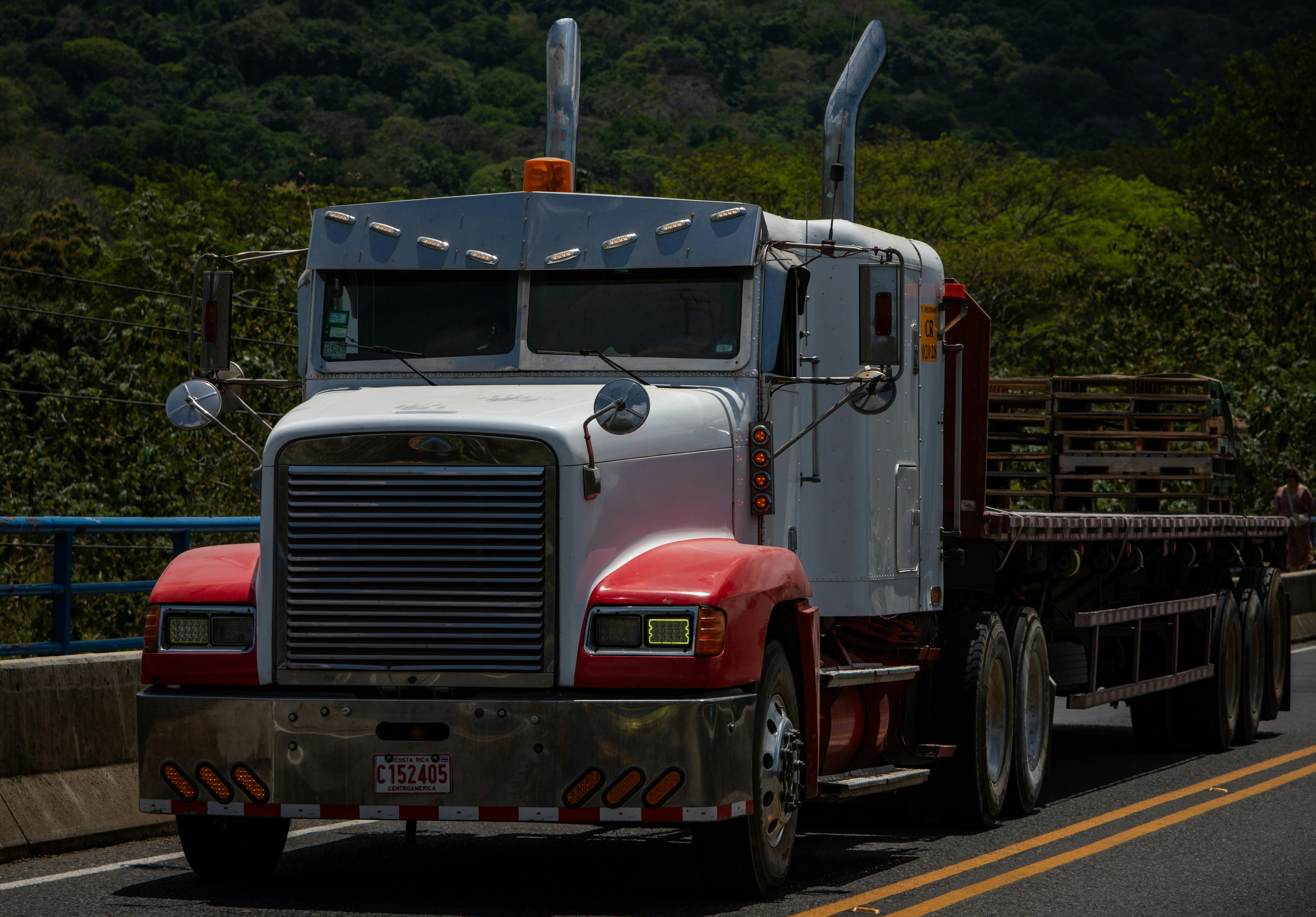 a semi truck driving down a road next to a forest