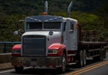 a semi truck driving down a road next to a forest