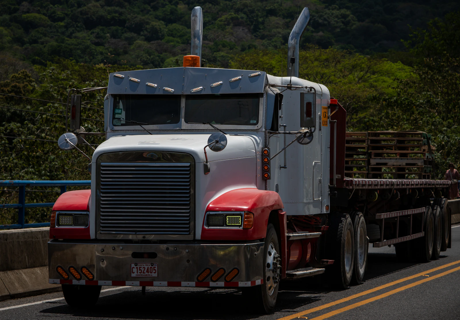 A semi truck driving down a road next to a forest