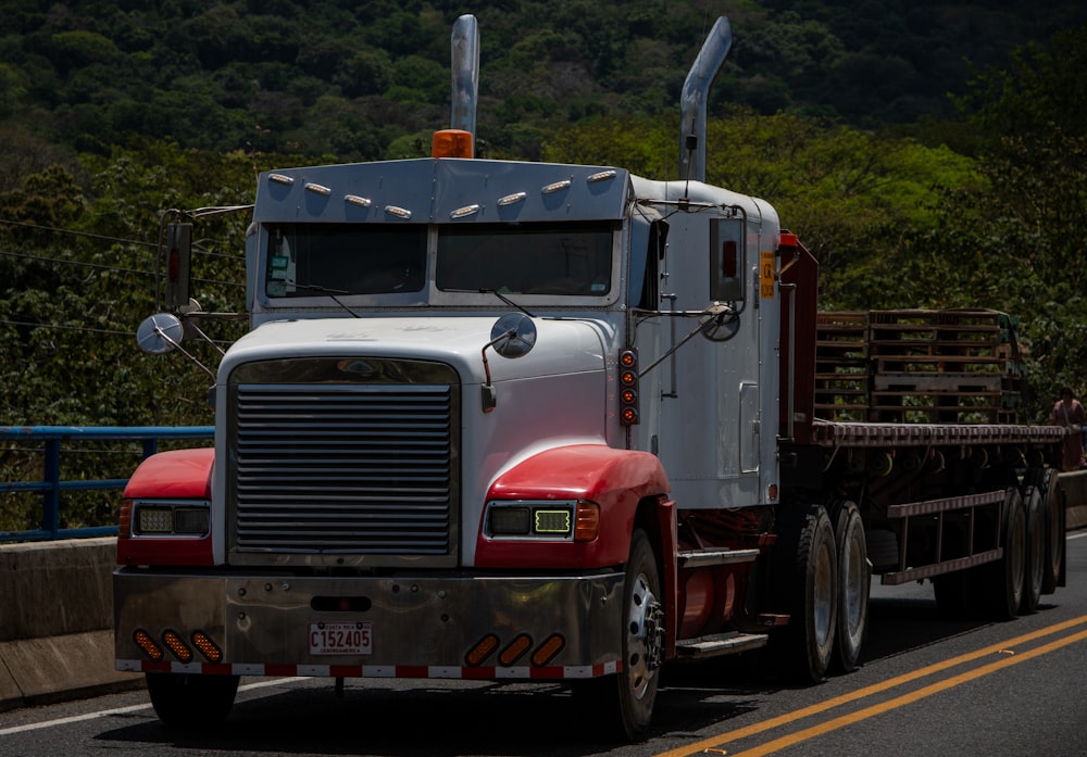 a semi truck driving down a road next to a forest