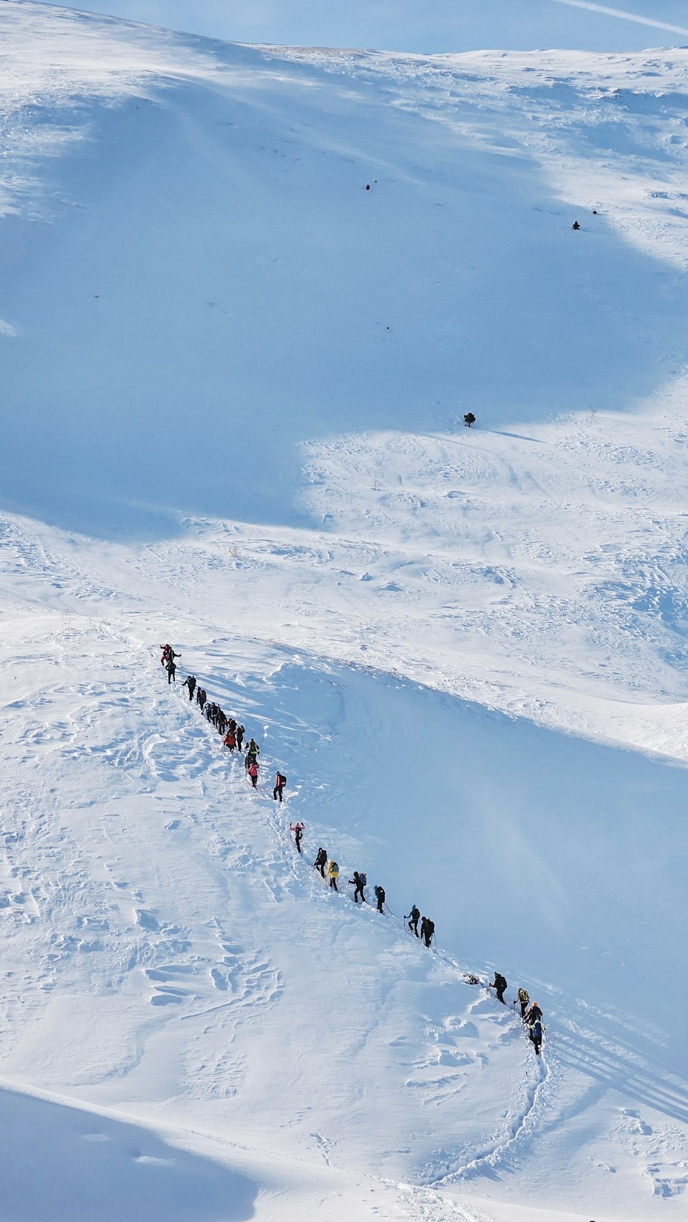 a long line of people walking across a snow covered slope