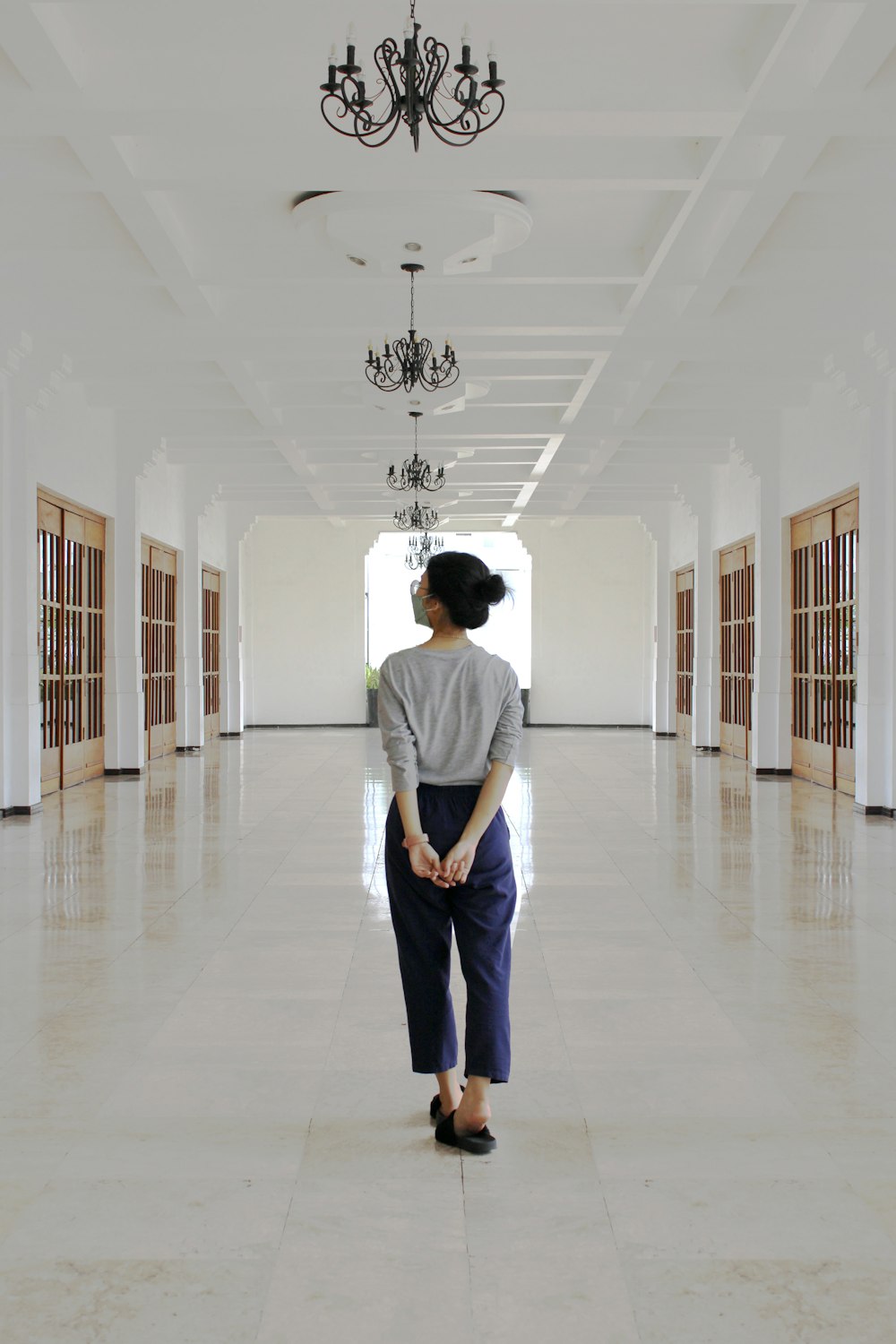 a woman standing in a hallway with a chandelier hanging from the ceiling