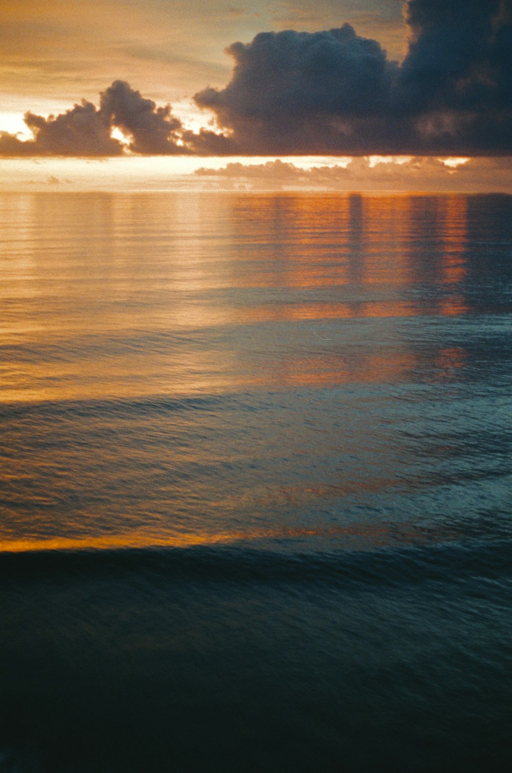 the sun is setting over the ocean with clouds in the sky