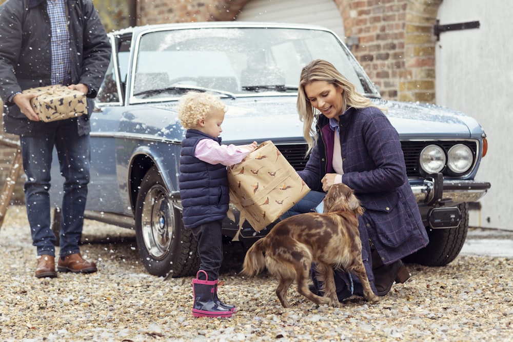 a woman and a child with two dogs in front of a car