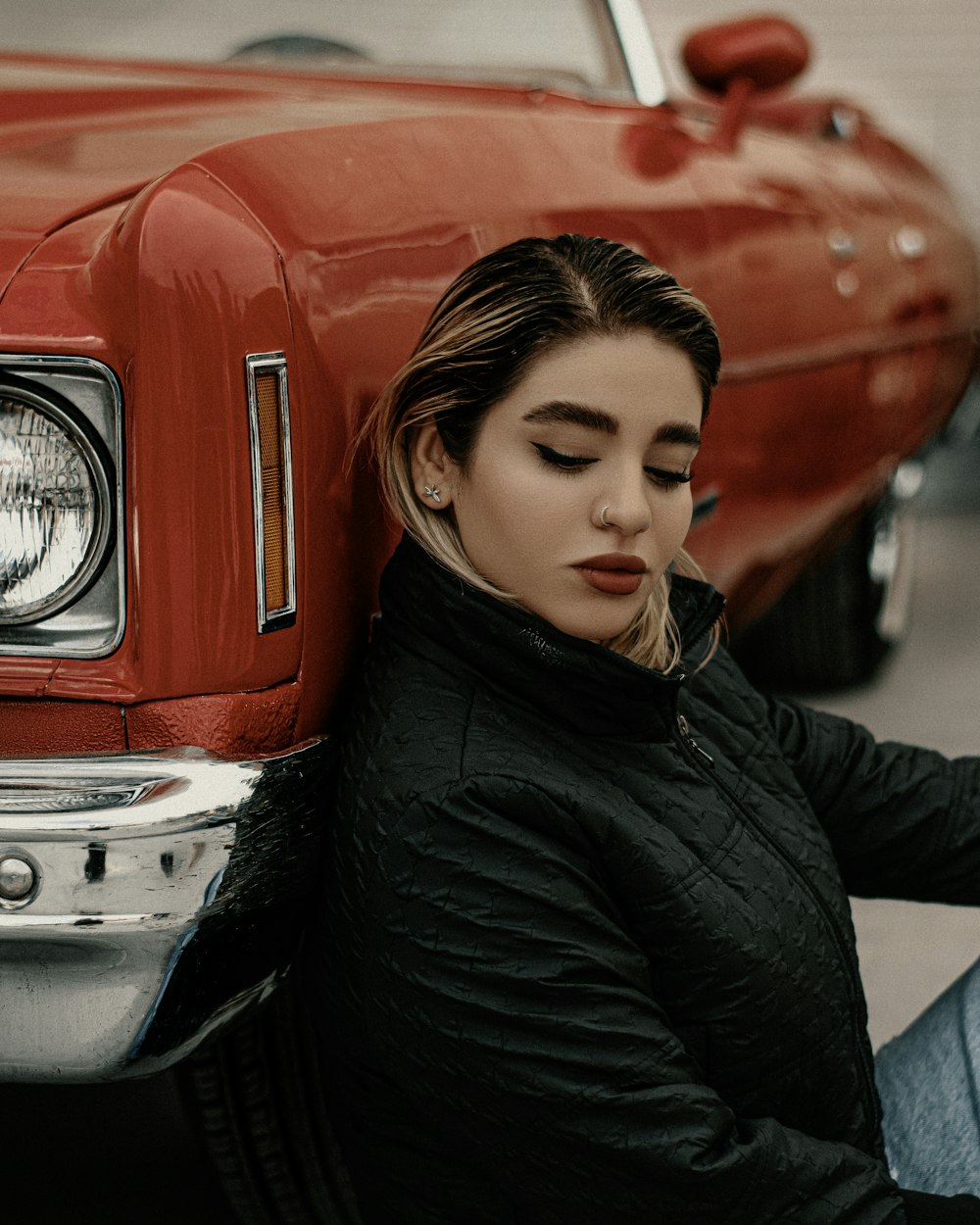 a woman sitting on the ground next to a red car