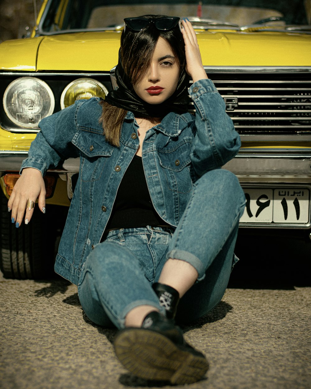 a woman sitting on the ground next to a yellow car