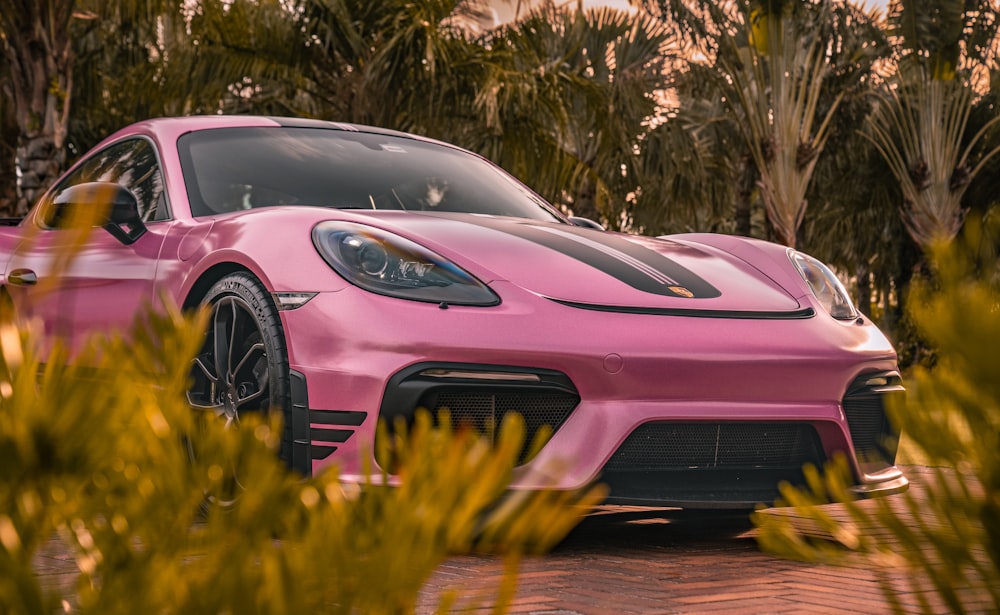 a pink sports car parked in front of some trees