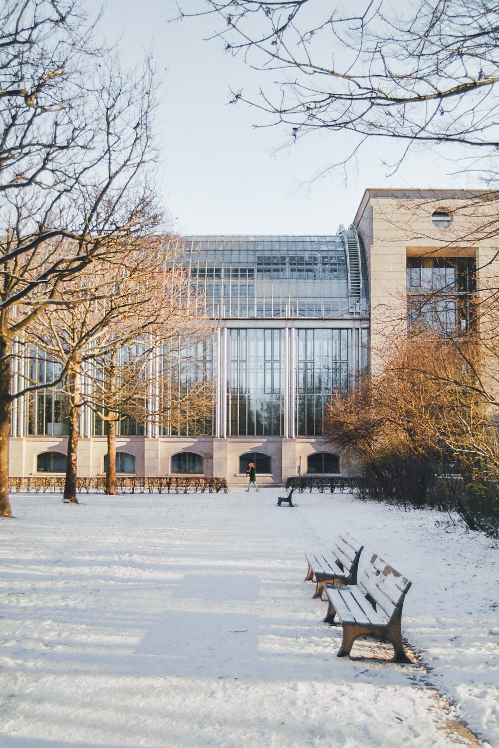 a snow covered park with benches and a building in the background
