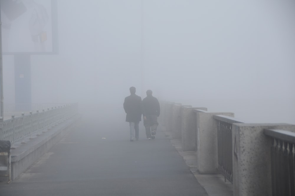 two people walking on a bridge in the fog