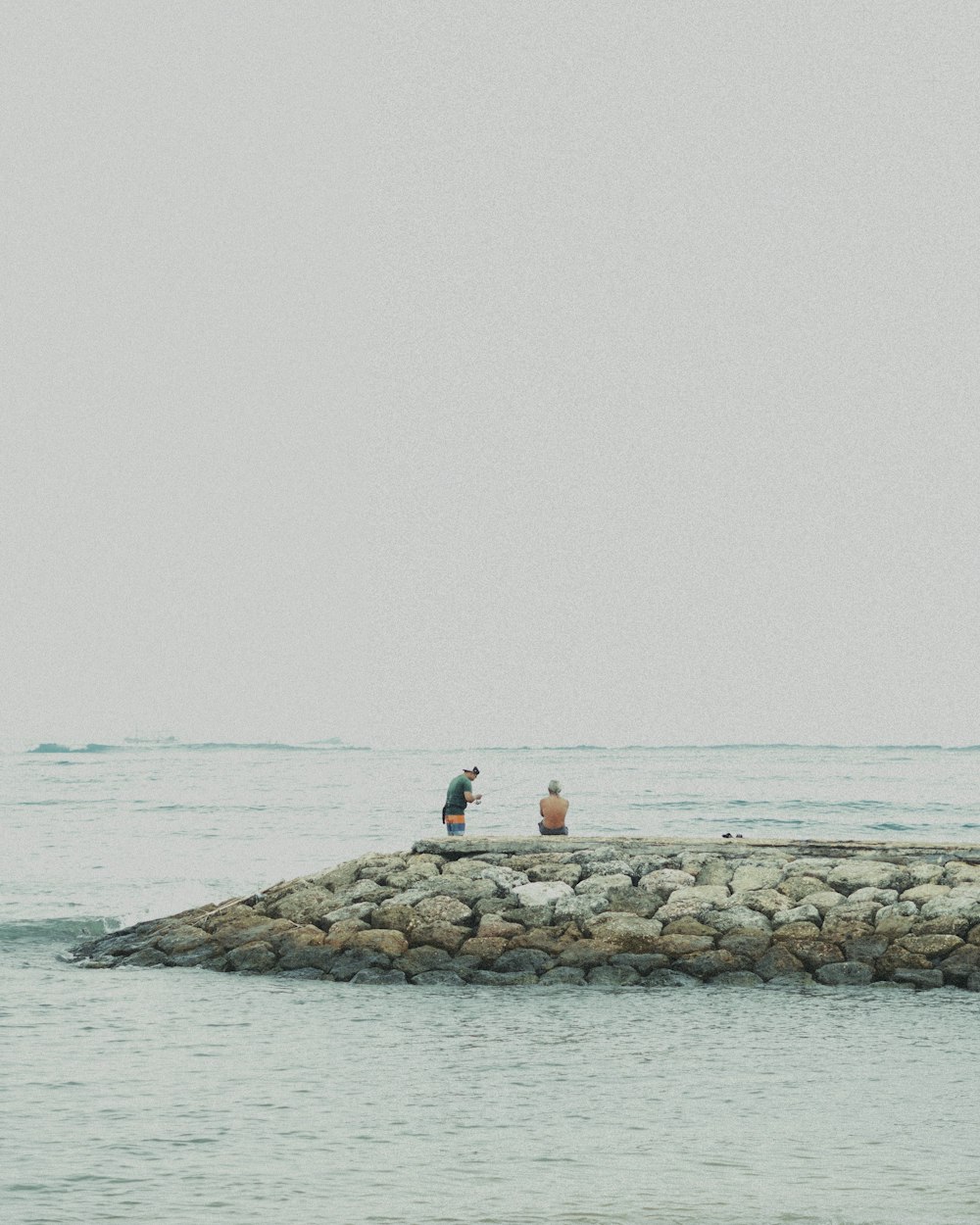 a couple of people standing on top of a rock pier