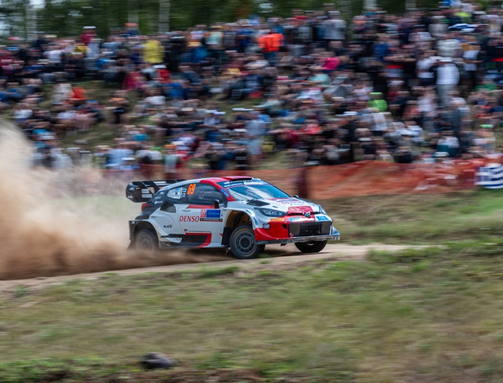 a rally car driving down a dirt road in front of a crowd