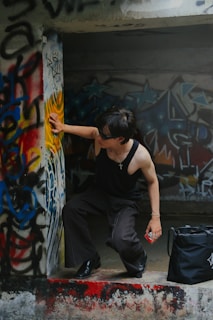 a man squatting on the ground next to a wall with graffiti on it