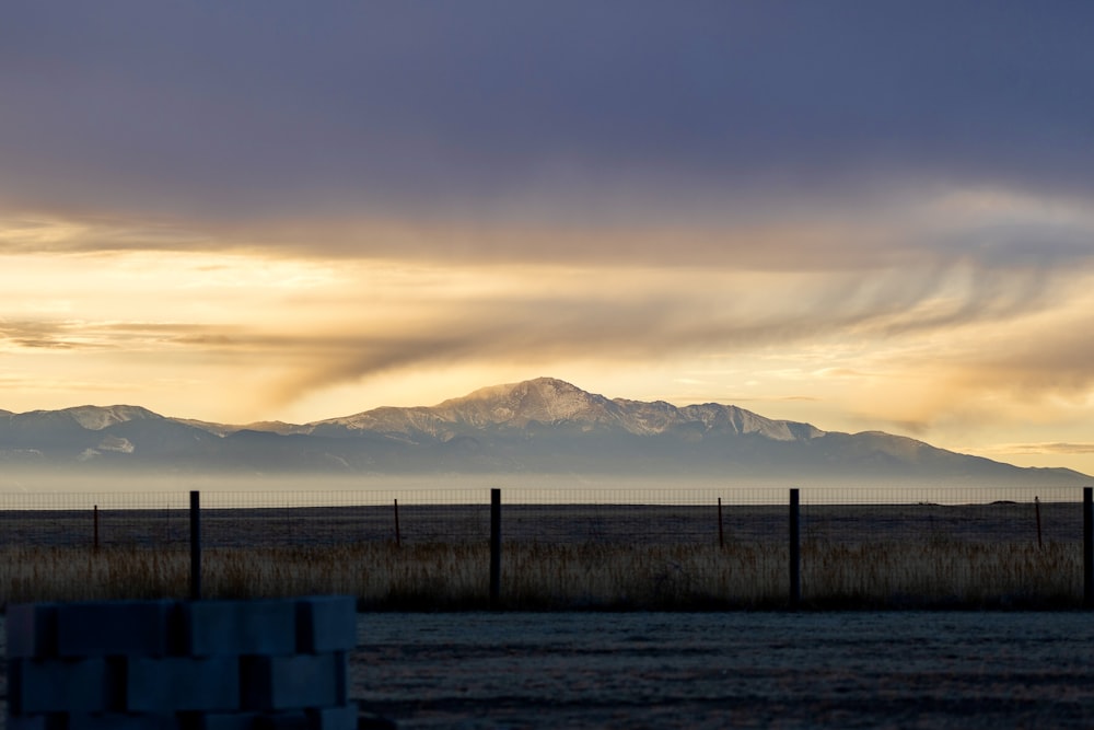 a field with a fence and mountains in the background