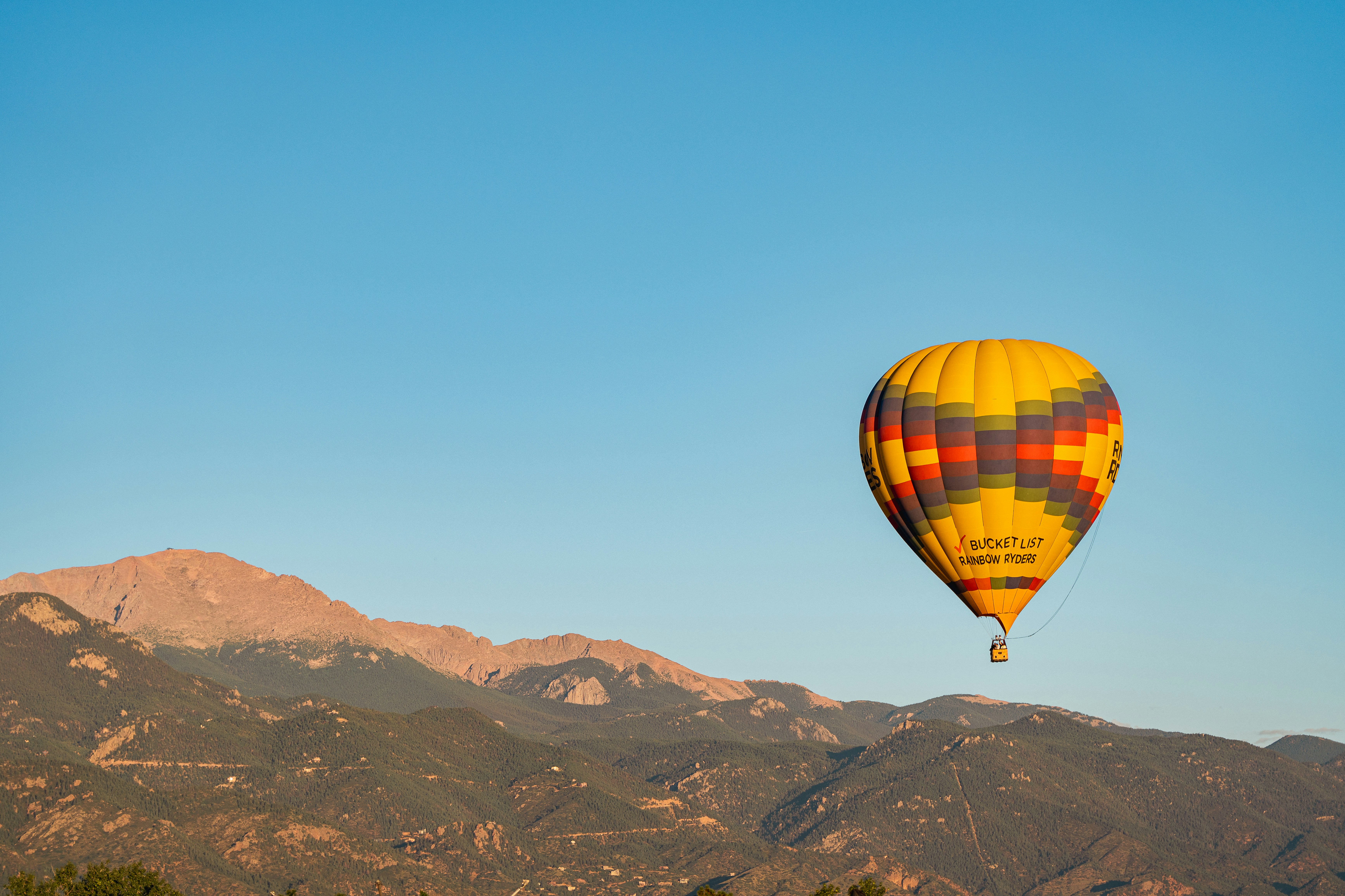 a hot air balloon flying over a mountain range, 
