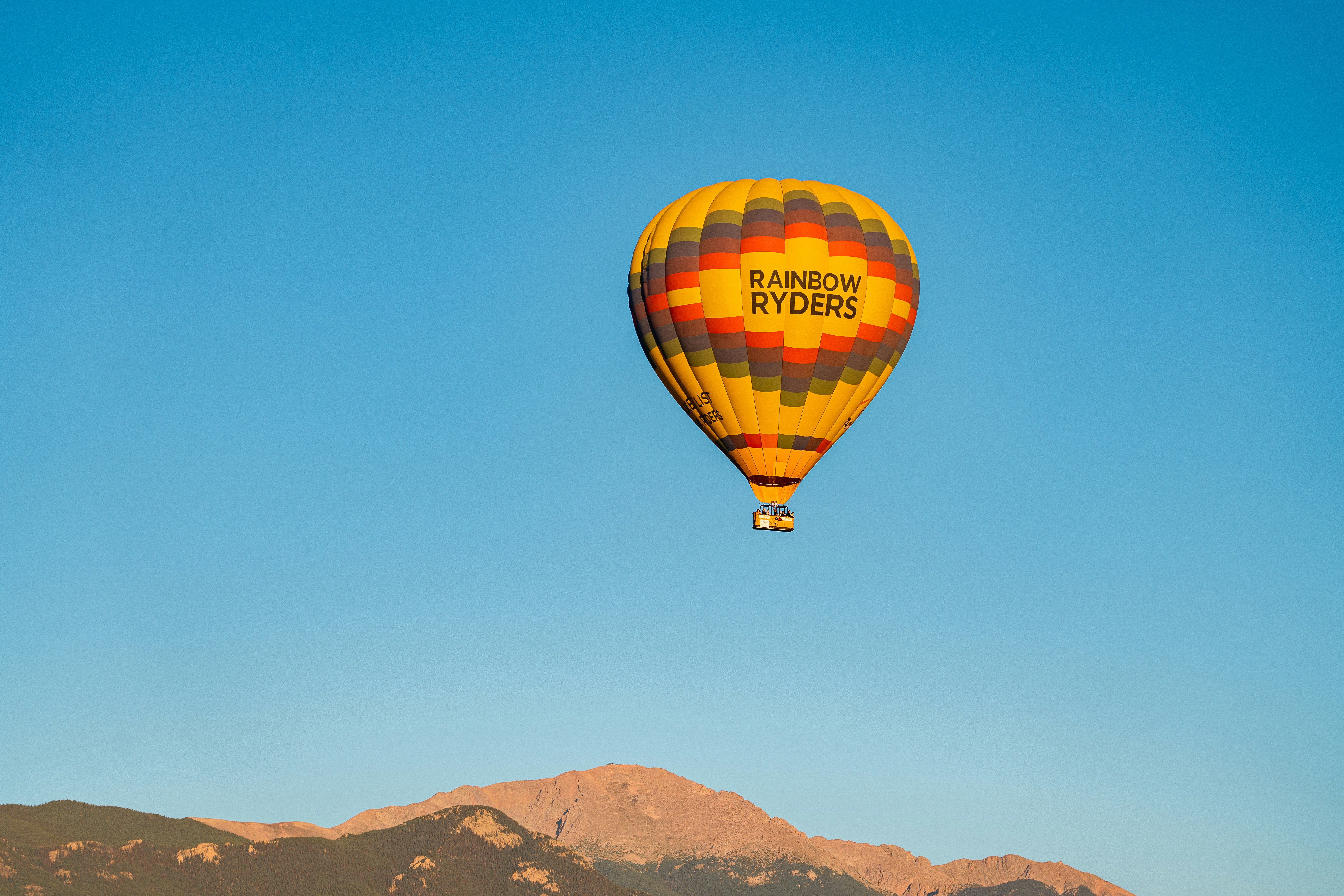 a hot air balloon flying over a mountain range, 