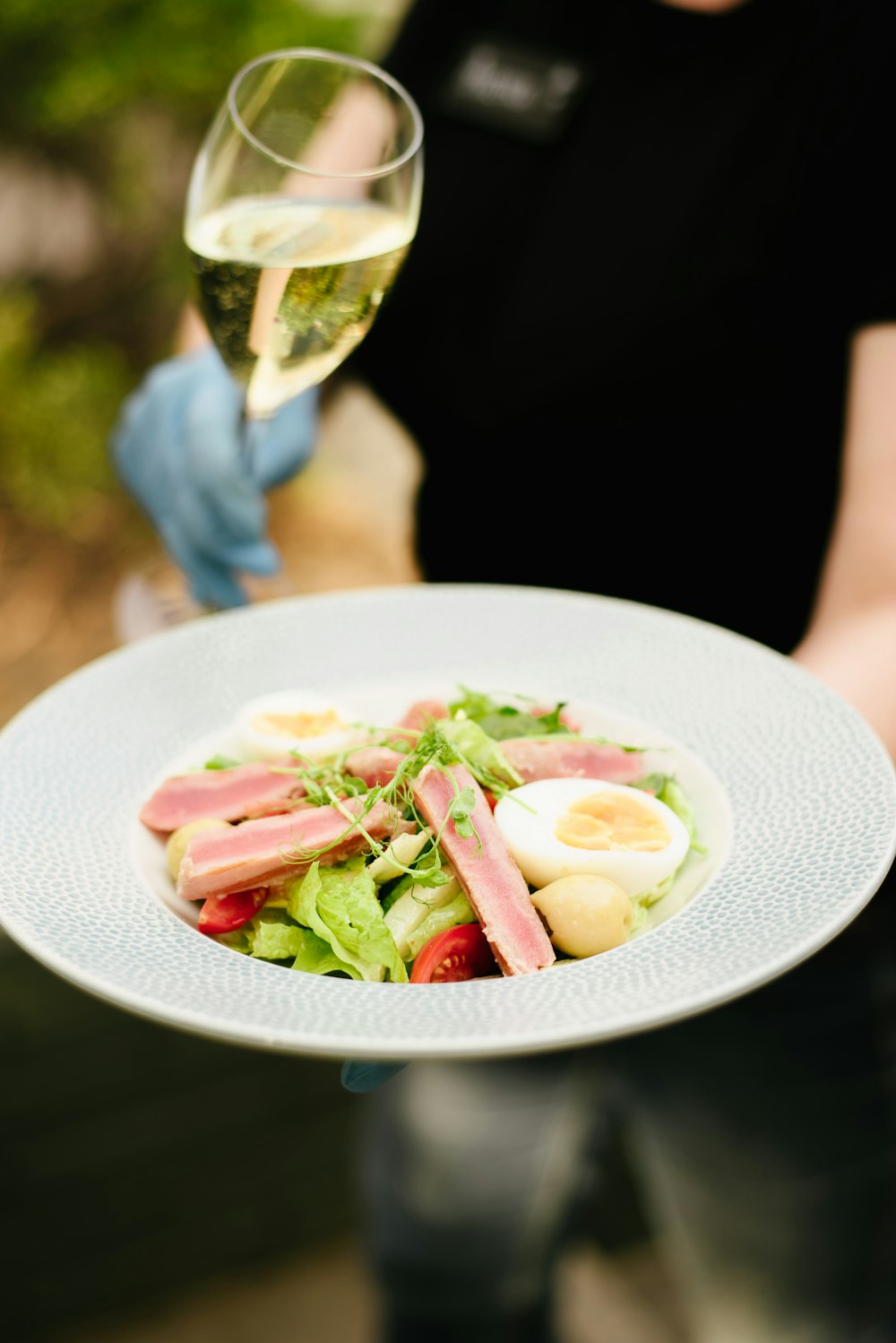 a person holding a plate of food and a glass of wine