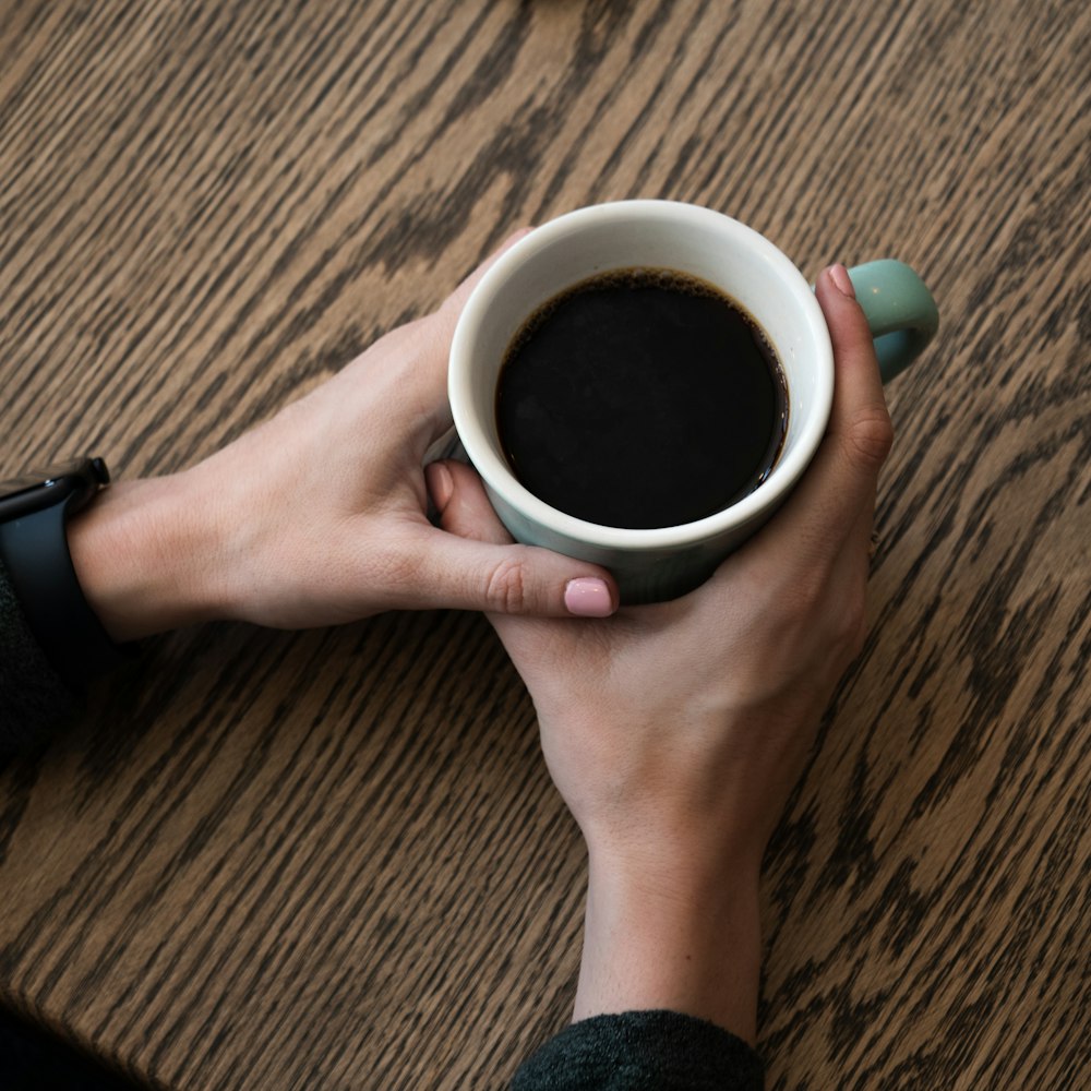 a person holding a cup of coffee on top of a wooden table