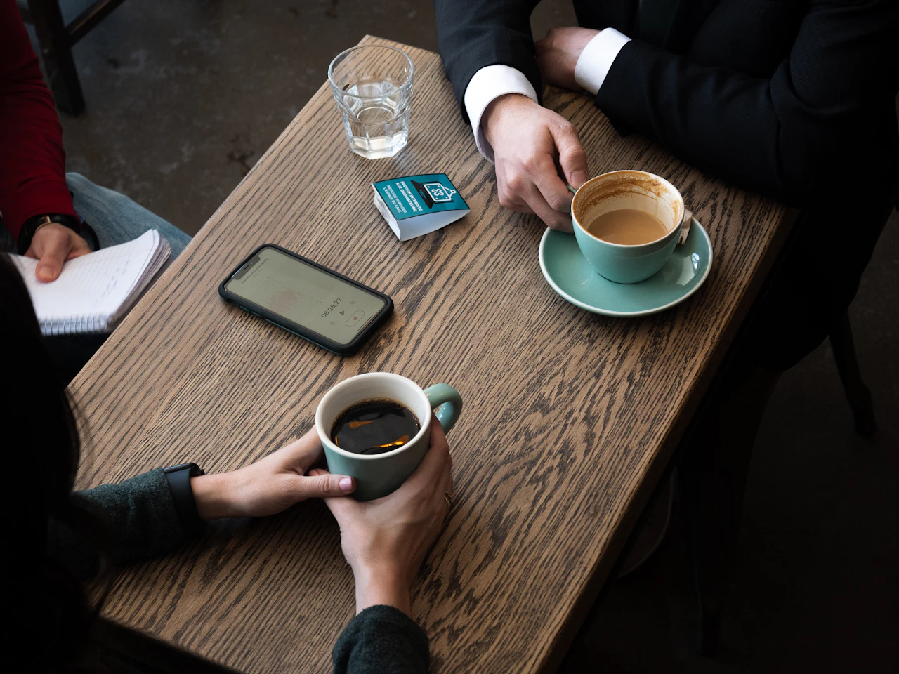 Two coffee cups and a notebook on a wooden café table