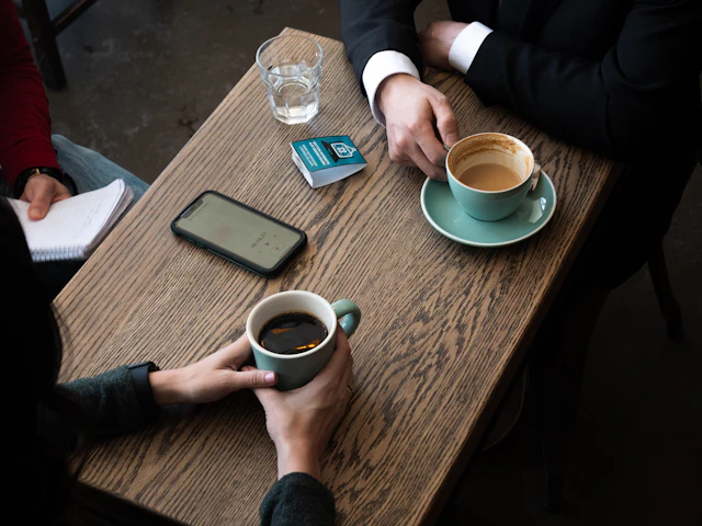 Two coffee cups and a notebook on a wooden café table