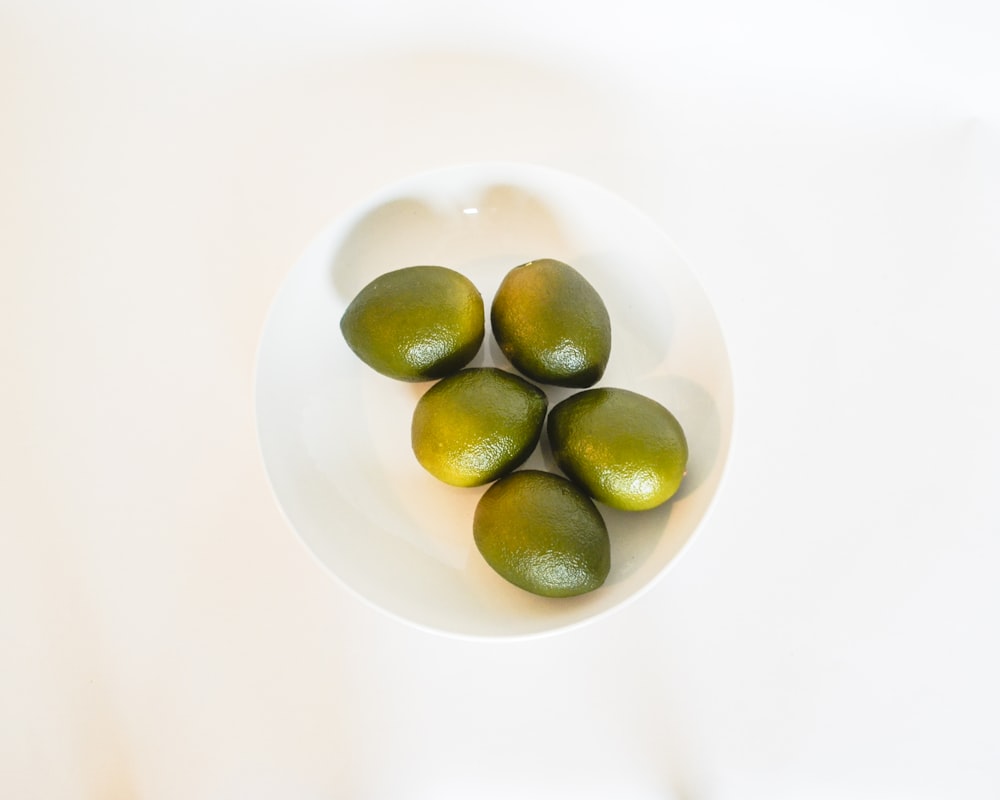 un bol blanc rempli de citrons verts sur le dessus d’une table