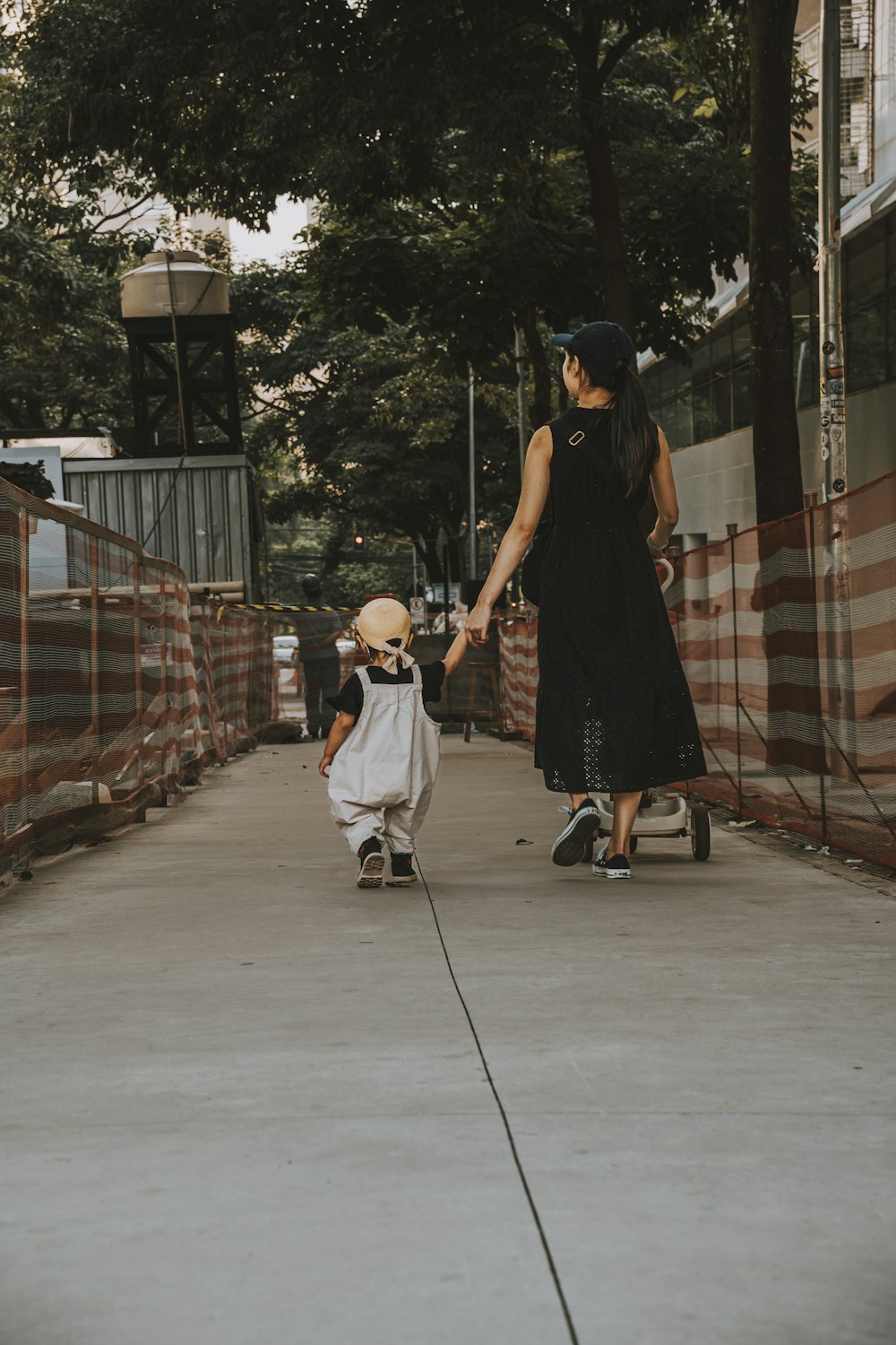a woman and a child holding hands walking down a sidewalk