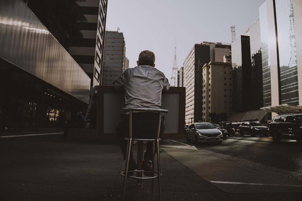 a man sitting on a stool in the middle of a city