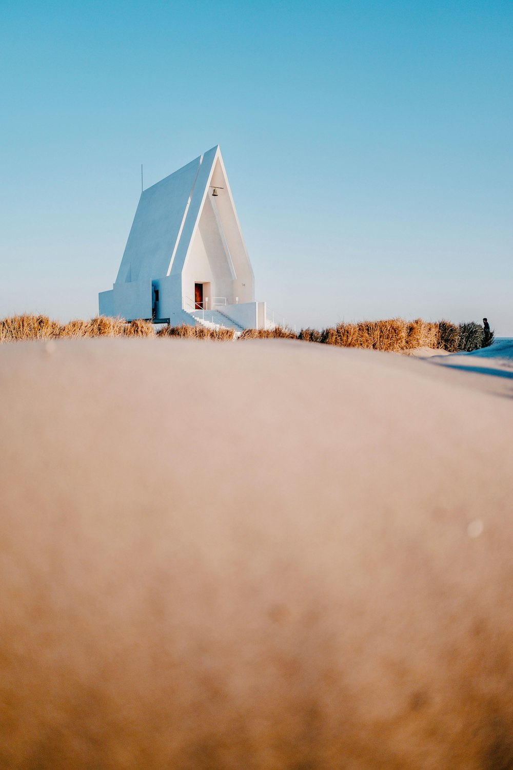 a white building with a red door sitting on top of a beach