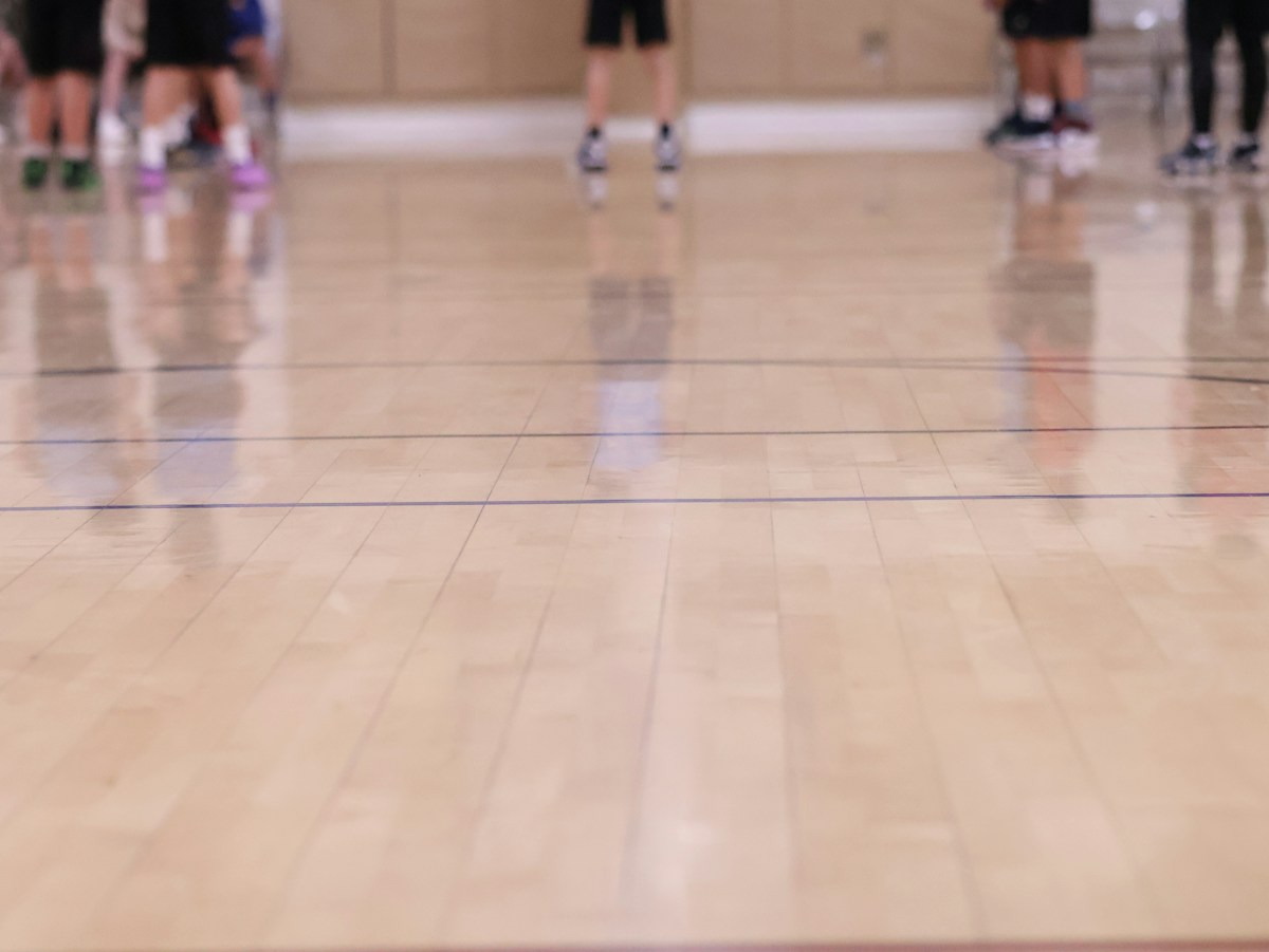 Teens playing basketball in a high school gym, practicing teamwork and skills during a PE class game.
