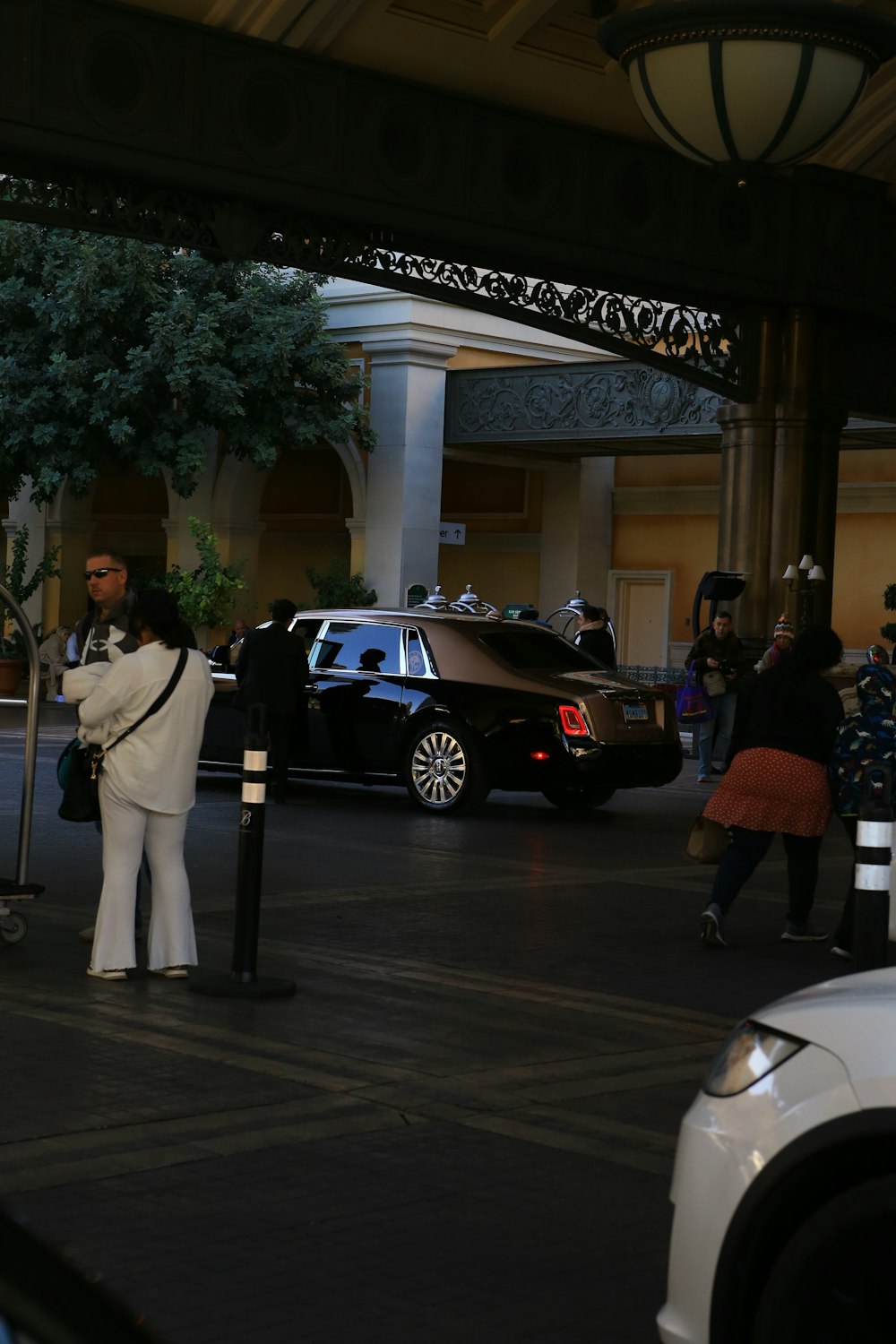 a man in a white suit standing next to a black car