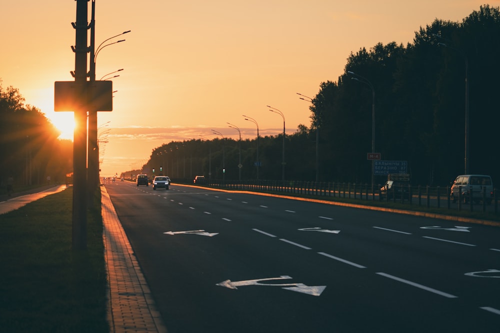 the sun is setting over a highway with cars driving down it
