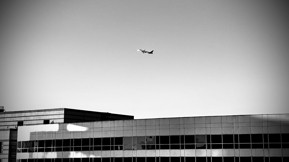 a black and white photo of an airplane flying over a building