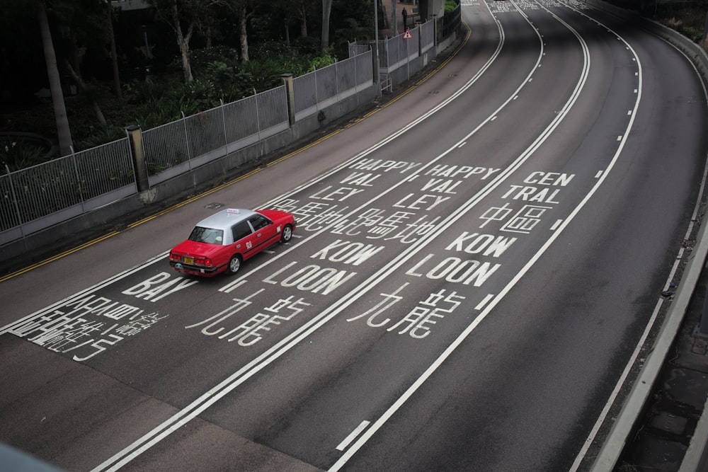 Une voiture rouge roulant dans une rue à côté d’un pont